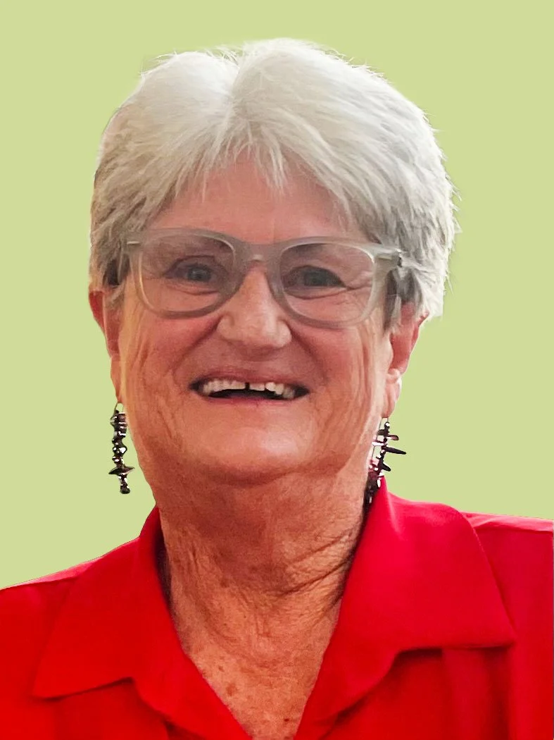 A smiling elderly woman with short white hair, wearing glasses, earrings, and a red shirt, against a light green background.