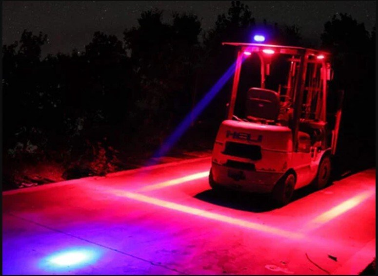 A forklift truck with red and blue emergency lights on a dark night, emitting red light onto the ground.