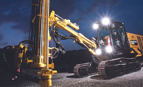 Large yellow CAT excavator with drilling attachment operating outdoors at night.
