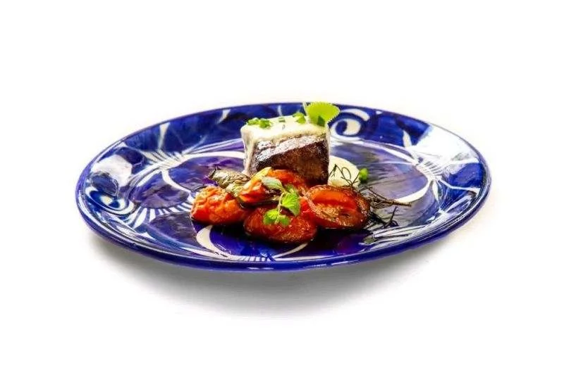 A plated fish dish with roasted tomatoes on a blue patterned plate.