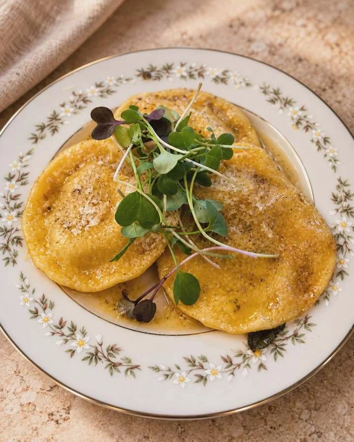 Ravioli with Parmesan, butter sauce, and microgreens on a floral plate.