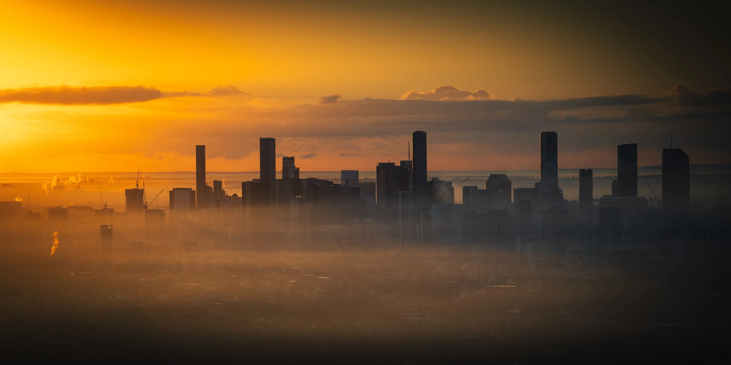 City skyline at sunset with tall buildings and a hazy foreground.