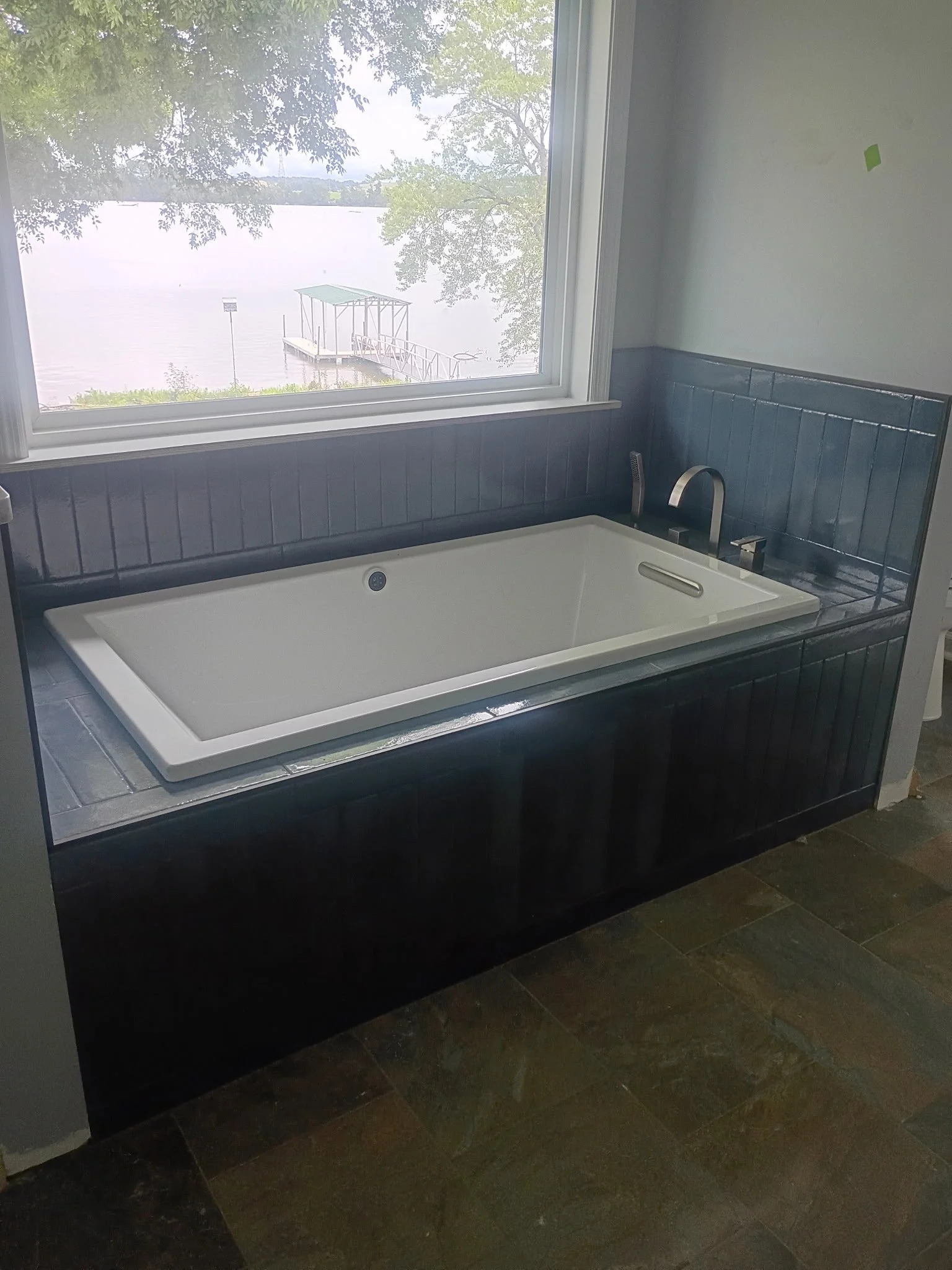 Indoor view of a bathtub with a view of a lake and dock outside the window.