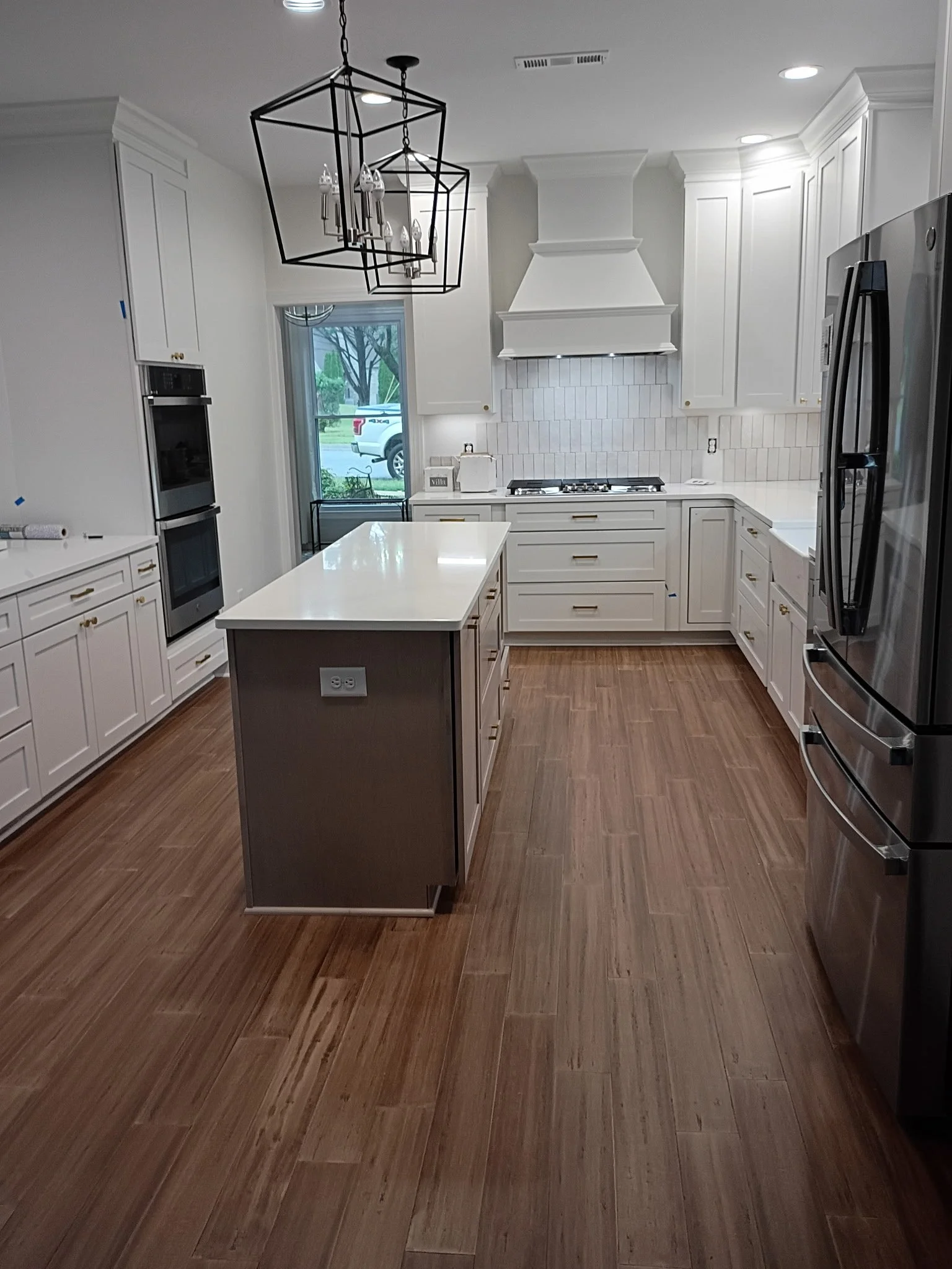 Modern kitchen with white cabinets, stainless steel appliances, a white island with electrical outlets, and dark hardwood flooring.