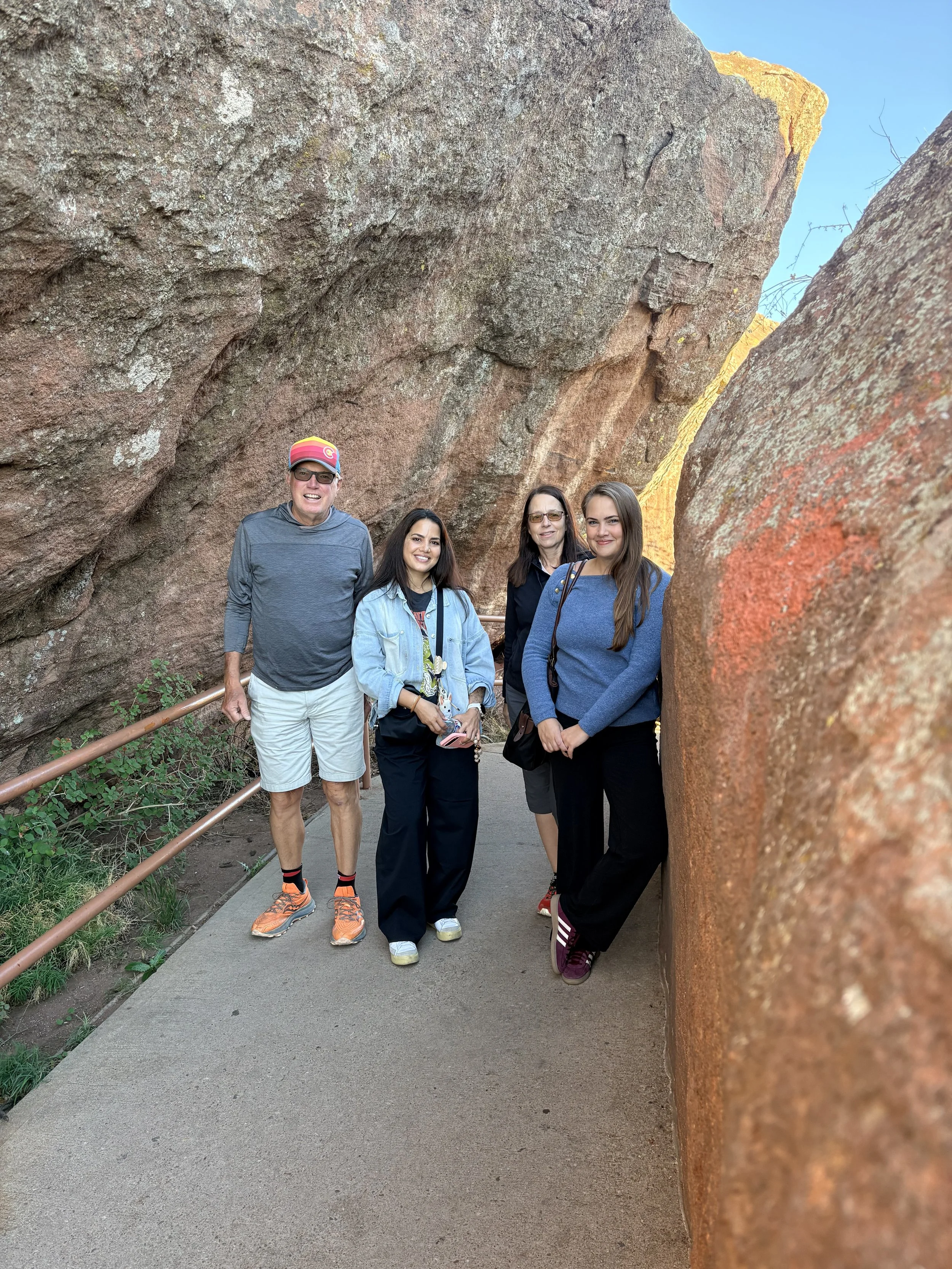 Four people standing in front of a large rock formation with a narrow gap, smiling at the camera.