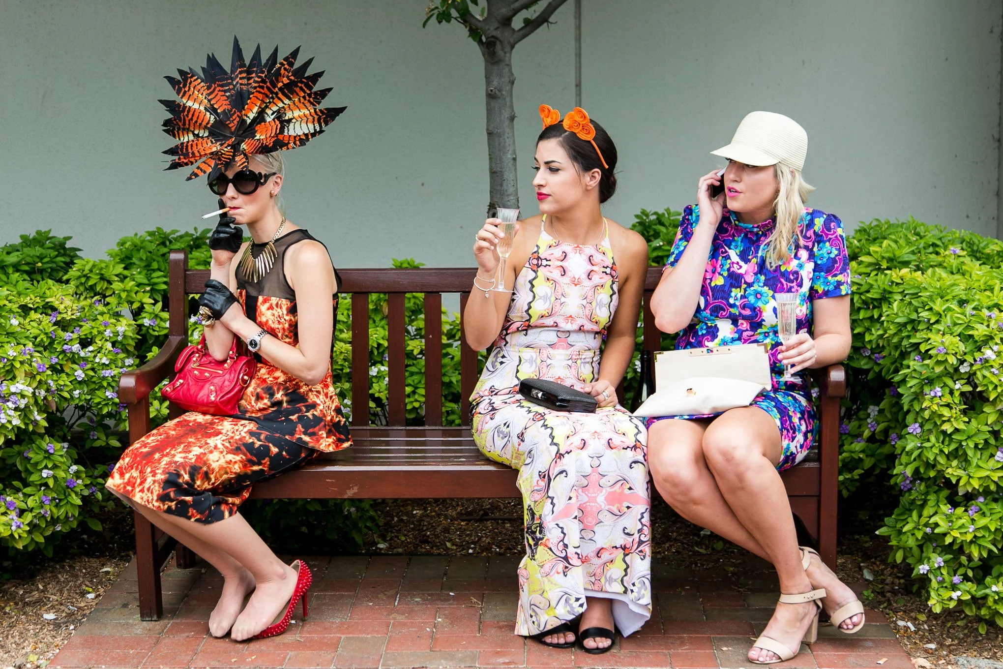 A woman wearing a colourful headpiece smokes a cigarette during Melbourne Cup Day at Flemington Racecourse.