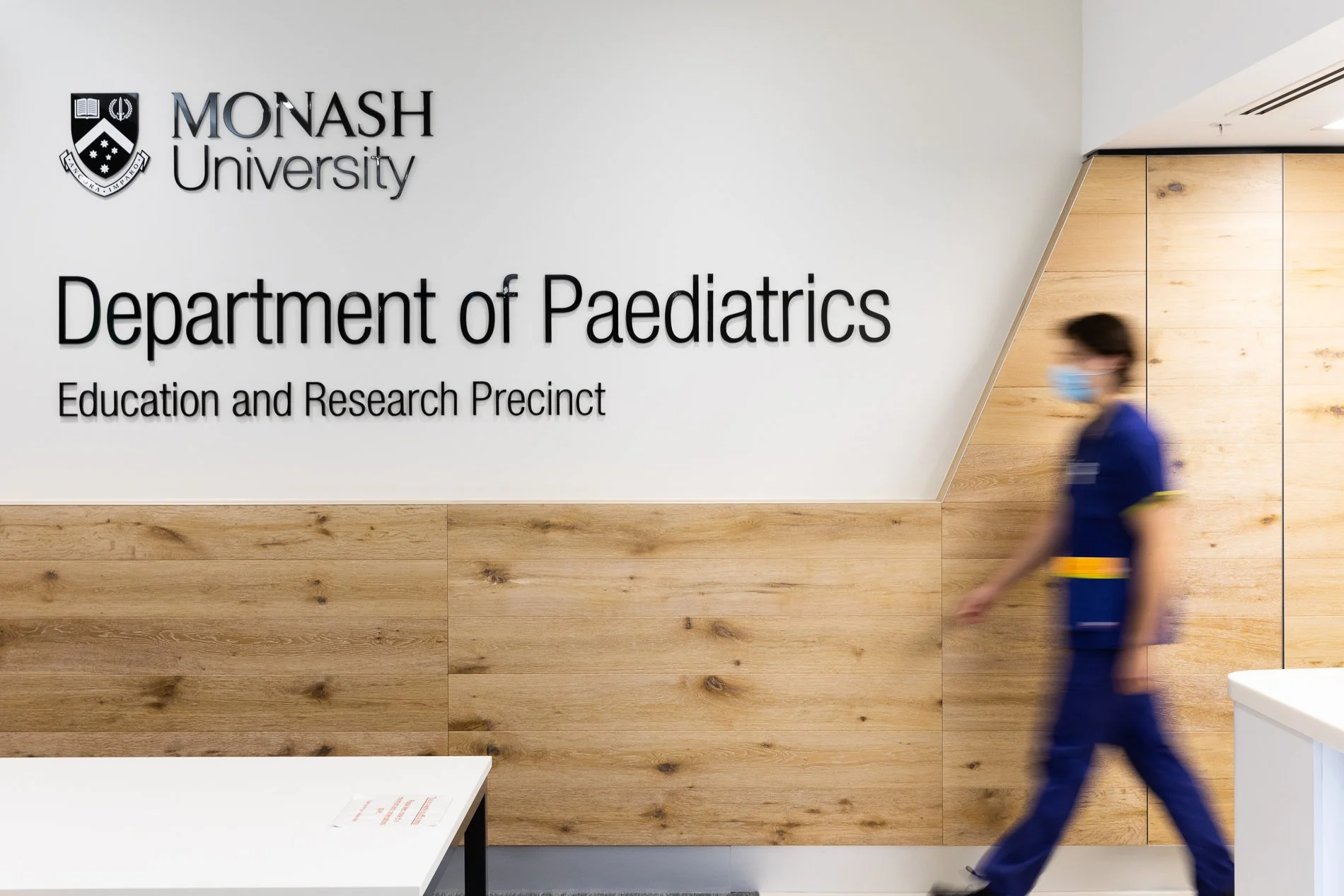 A healthcare worker walks past signage for the Monash University Department of Paediatrics Education and Research Precinct.