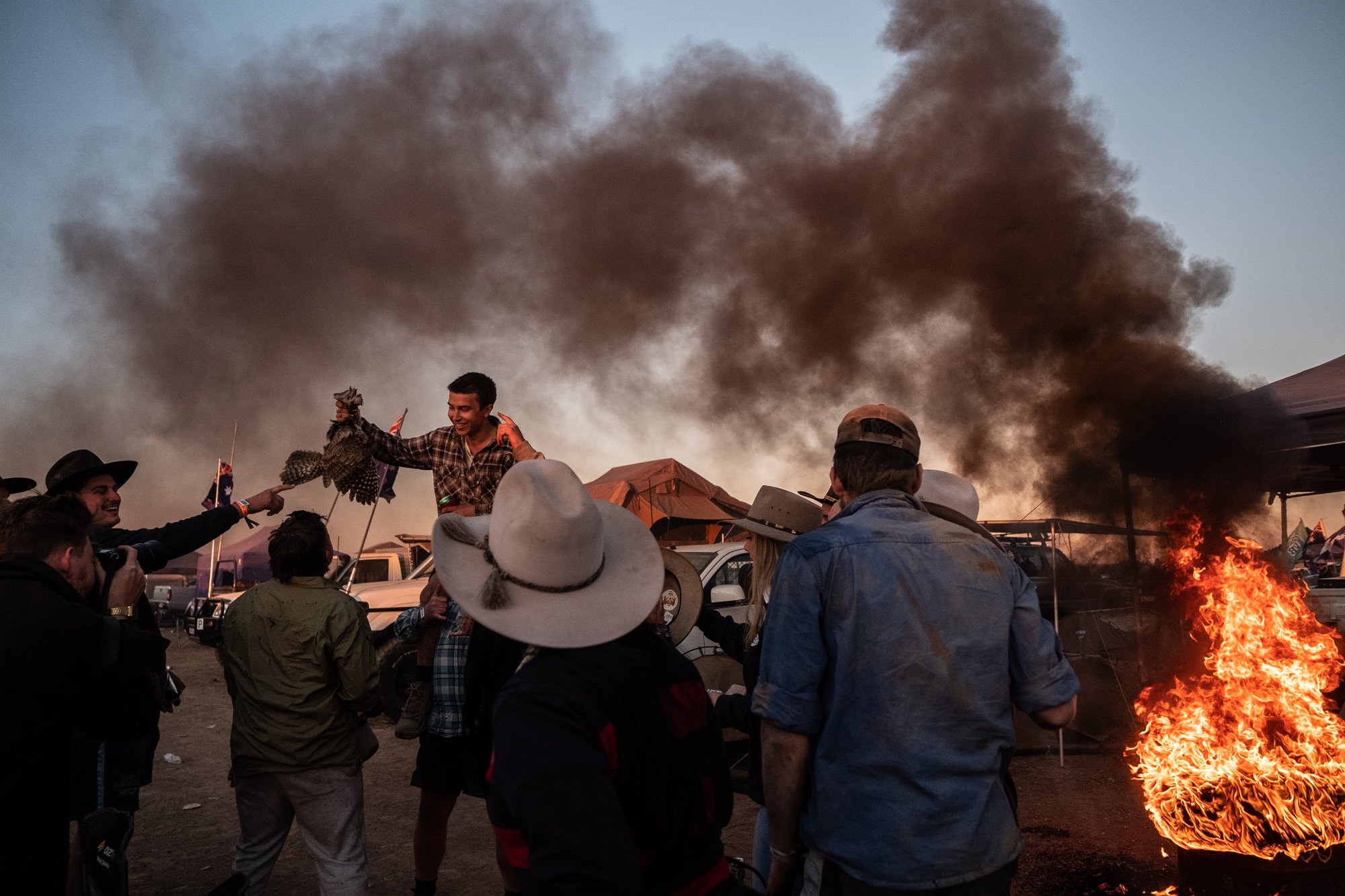 Friends gather around a smoking fire pit in the Ute paddock camping area during the Deniliquin Ute Muster.