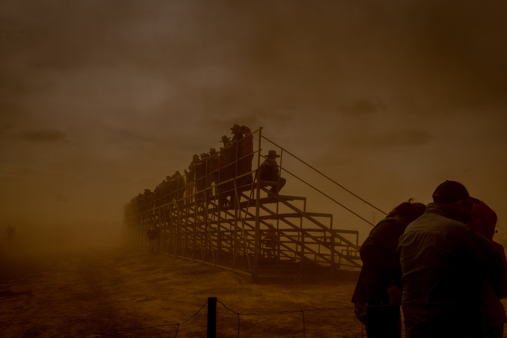 Spectators in the stands shield themselves from a large dust cloud 
