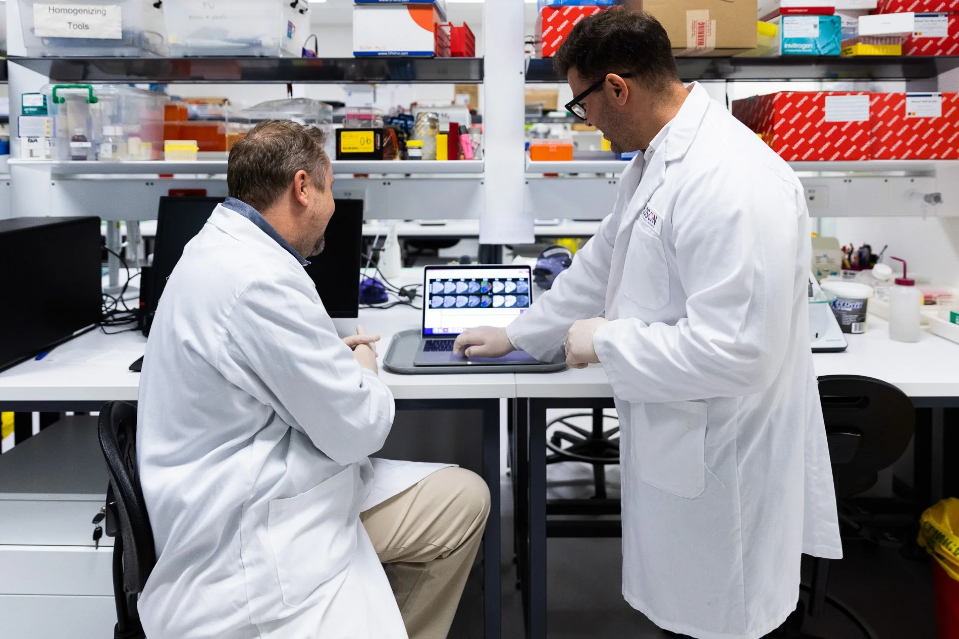 Two researchers in lab coats work together inside a university science laboratory.
