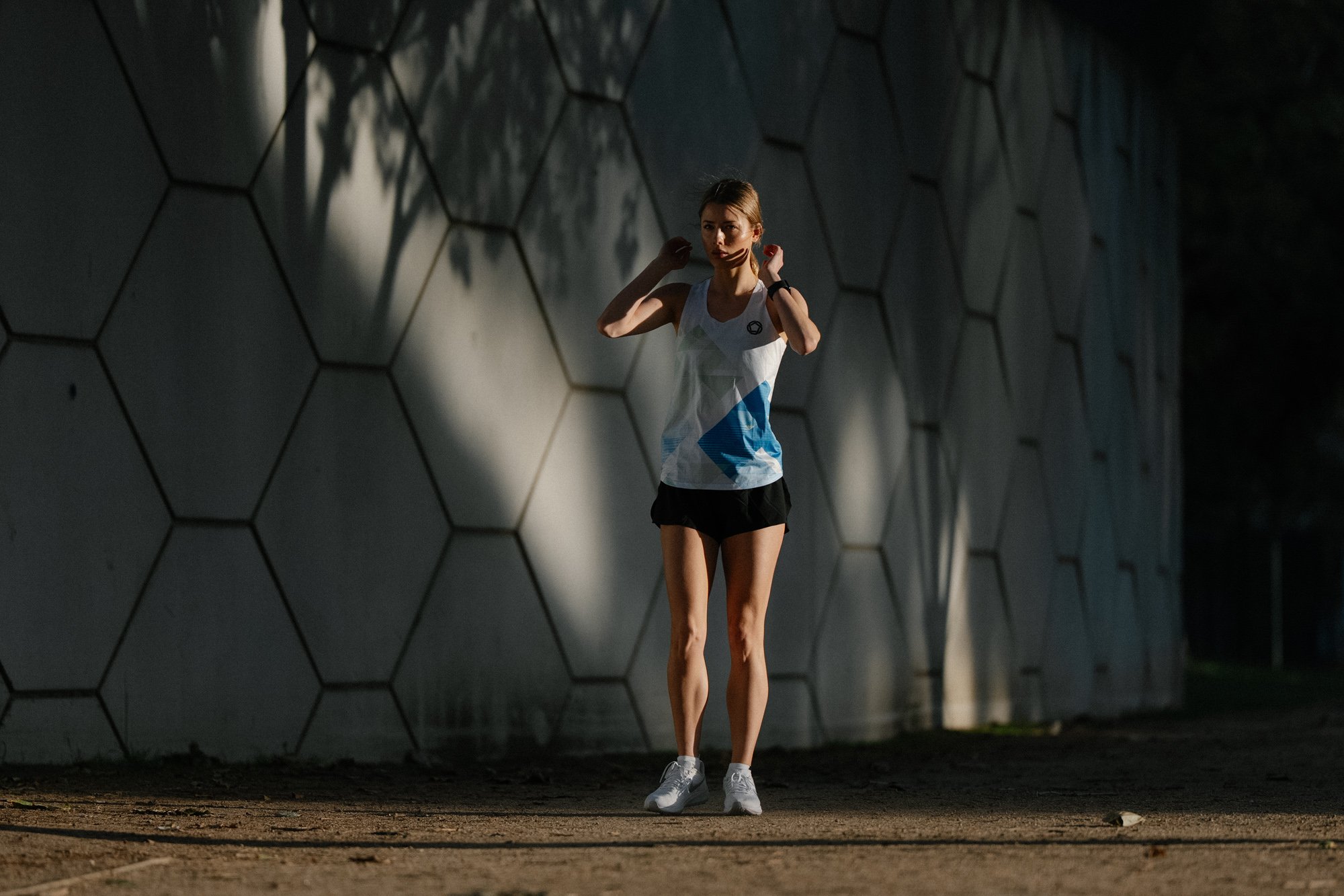 A woman runs beside an urban wall during a fitness lifestyle shoot.