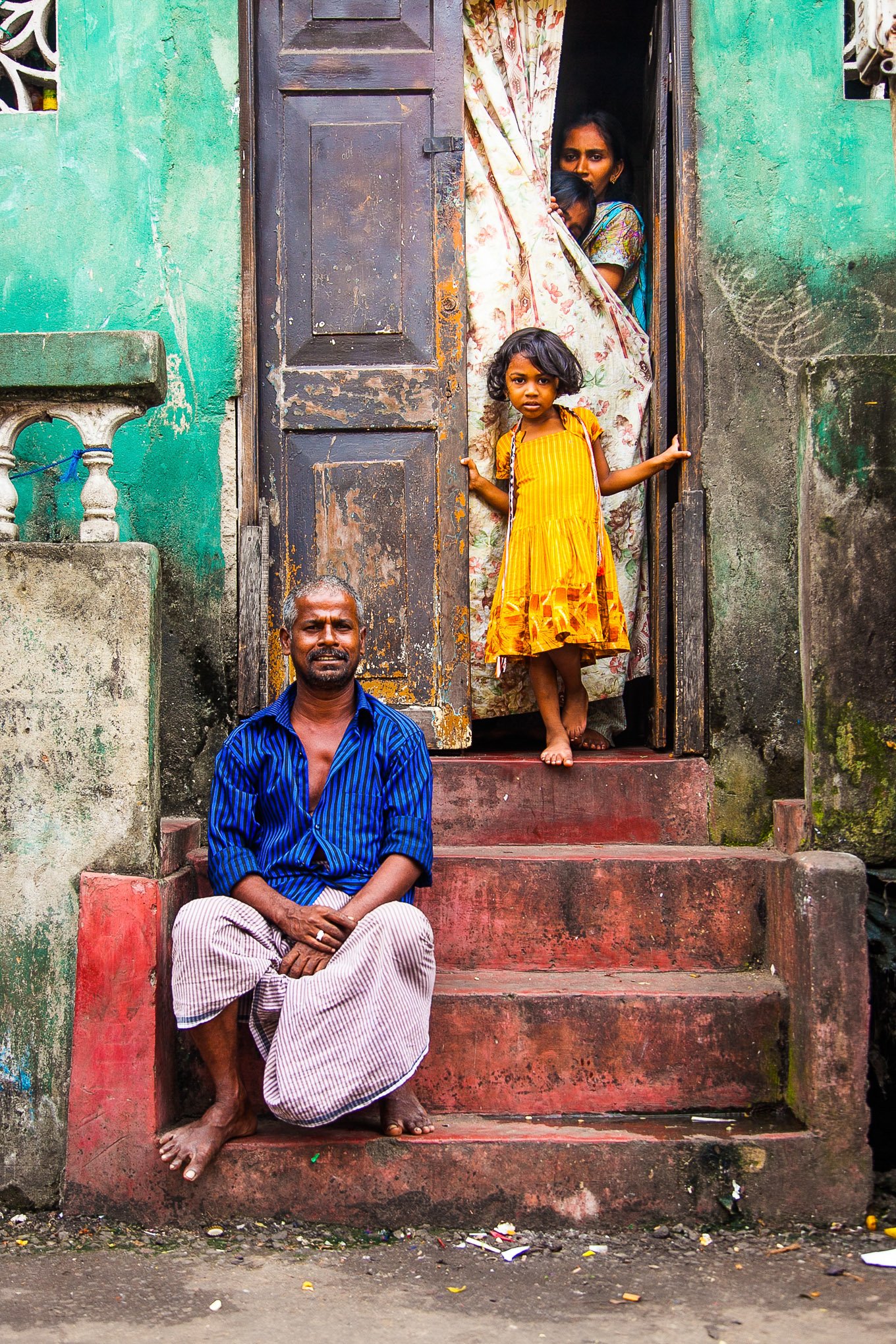 A portrait of a family, with the father sitting on the step & his daughters & wife by the door in Pettah Colombo Sri Lanka