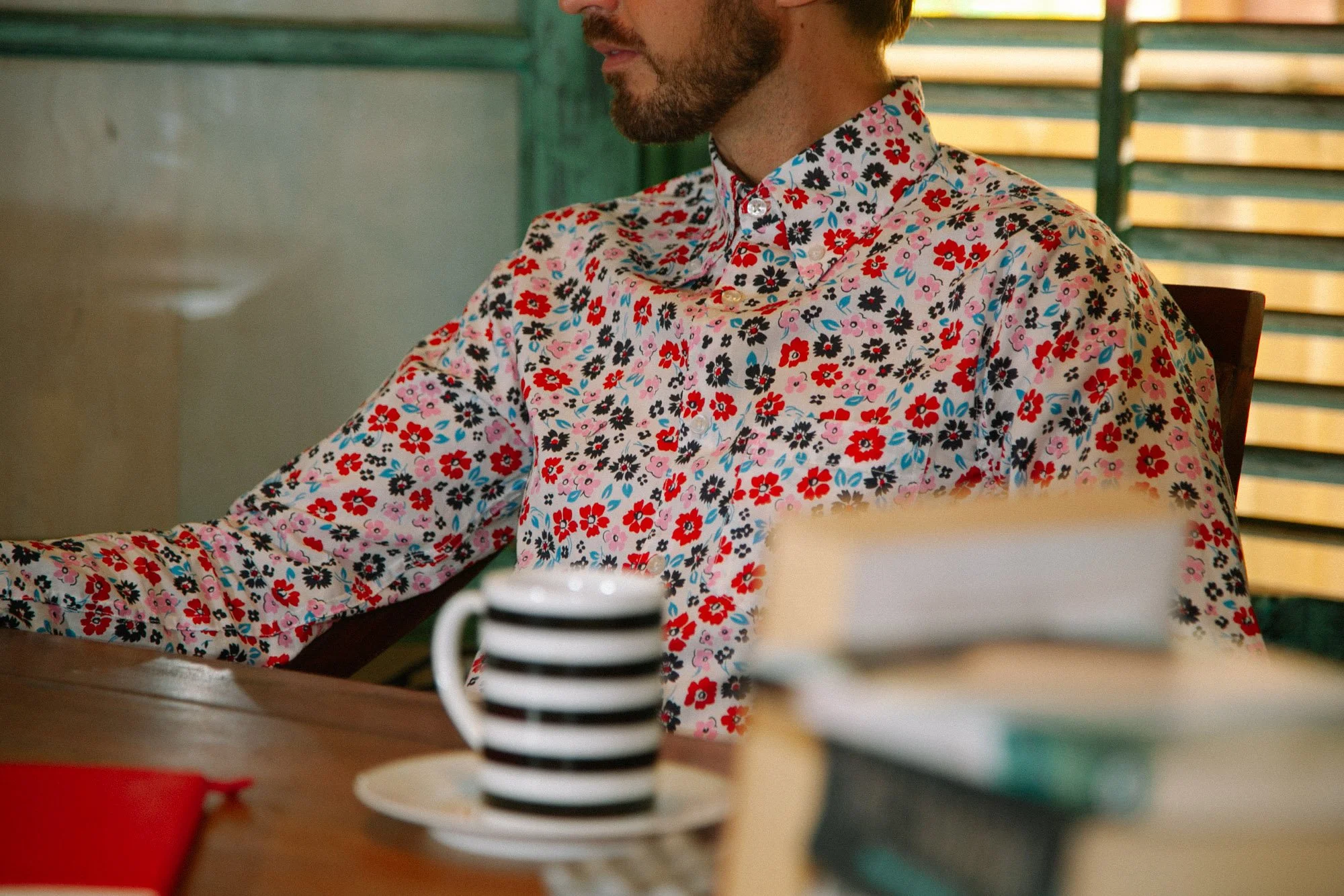 A man sits at a table with coffee and books during a relaxed lifestyle fashion shoot.