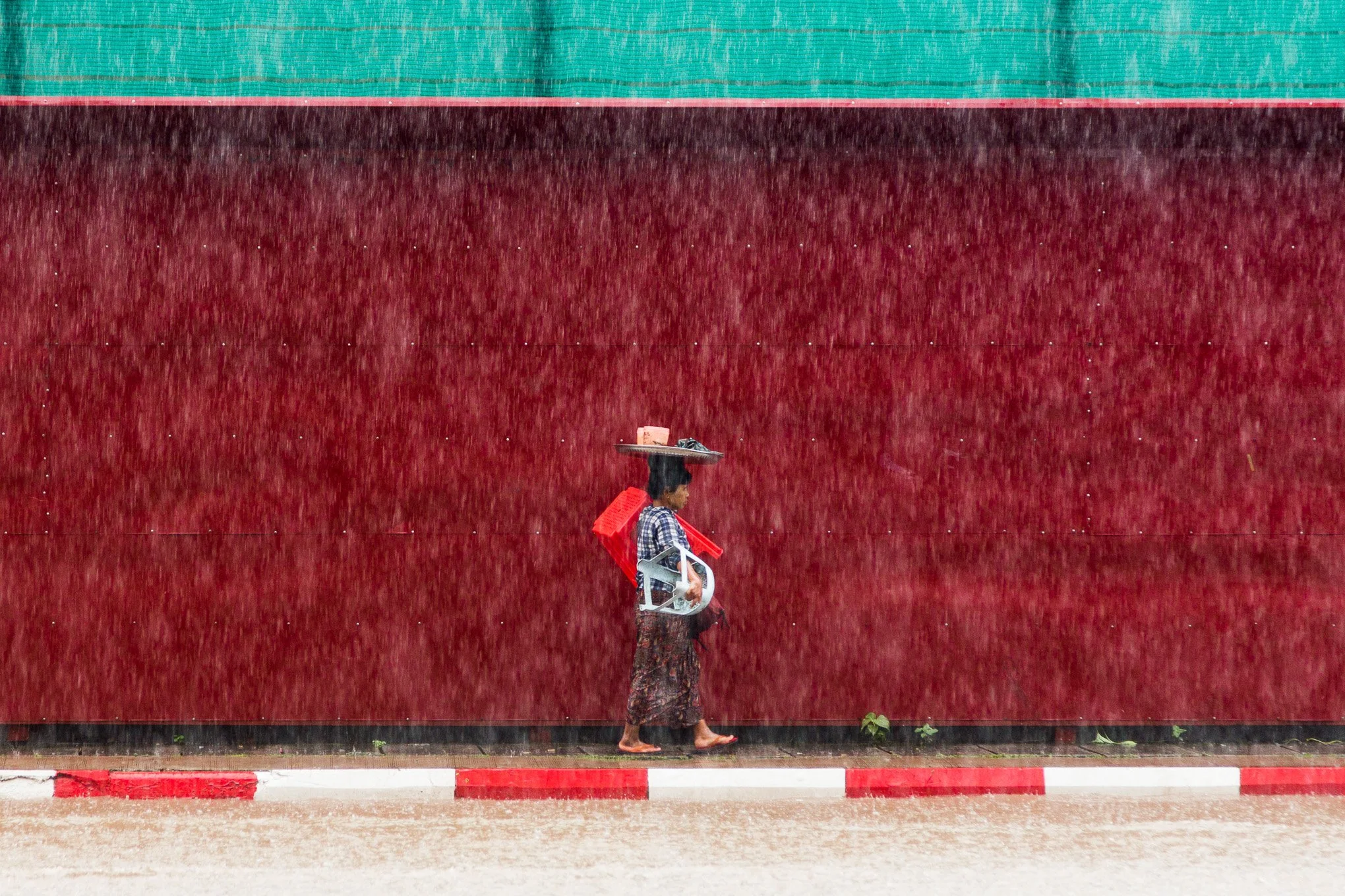 A street food hawker carries chairs and utensils through monsoon rain in Yangon.