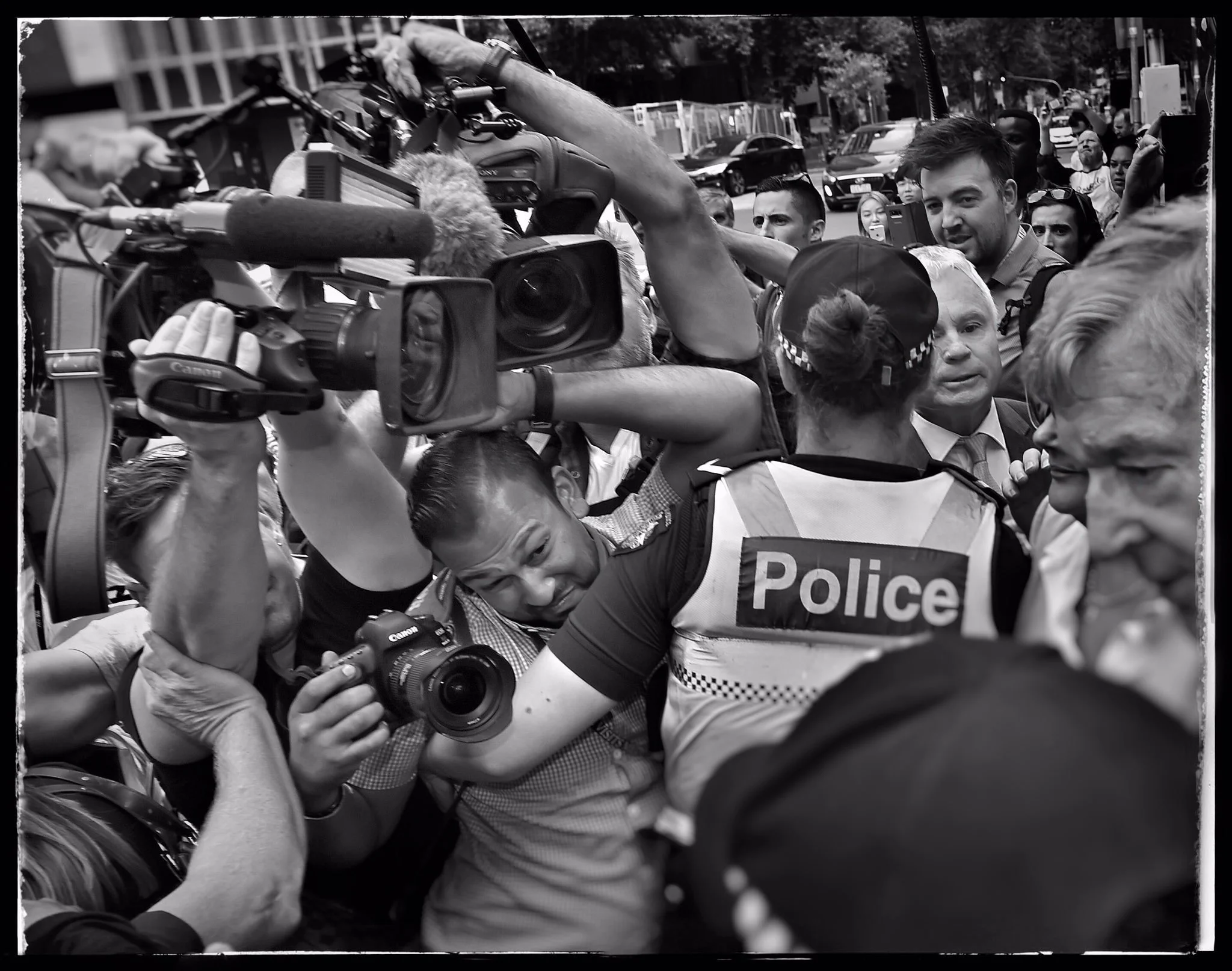 Photojournalist Asanka Brendon Ratnayake is held back by a police officer while photographing Cardinal George Pell in a crowded media scrum.