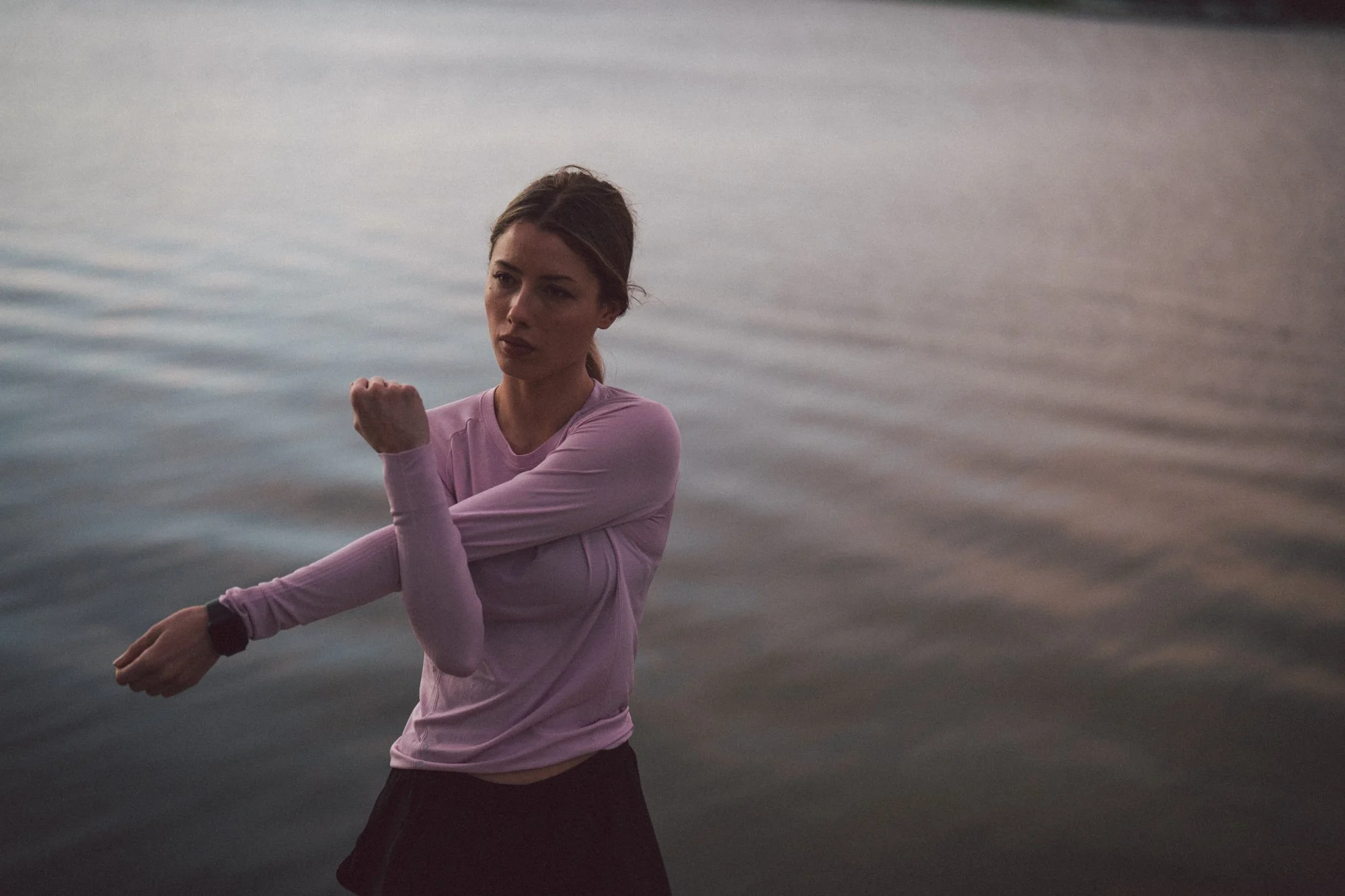 A woman warms up beside water during an outdoor running shoot.