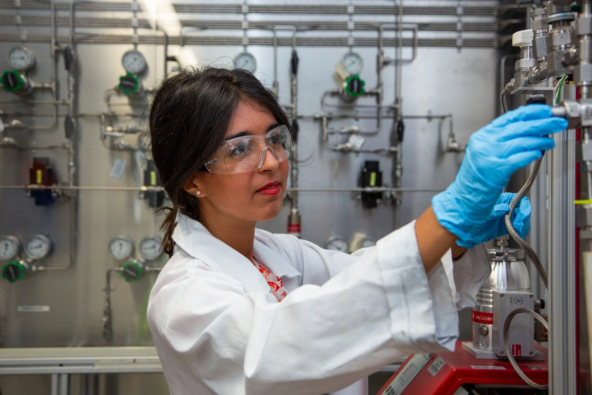 A researcher wearing safety glasses adjusts equipment inside a university science laboratory.