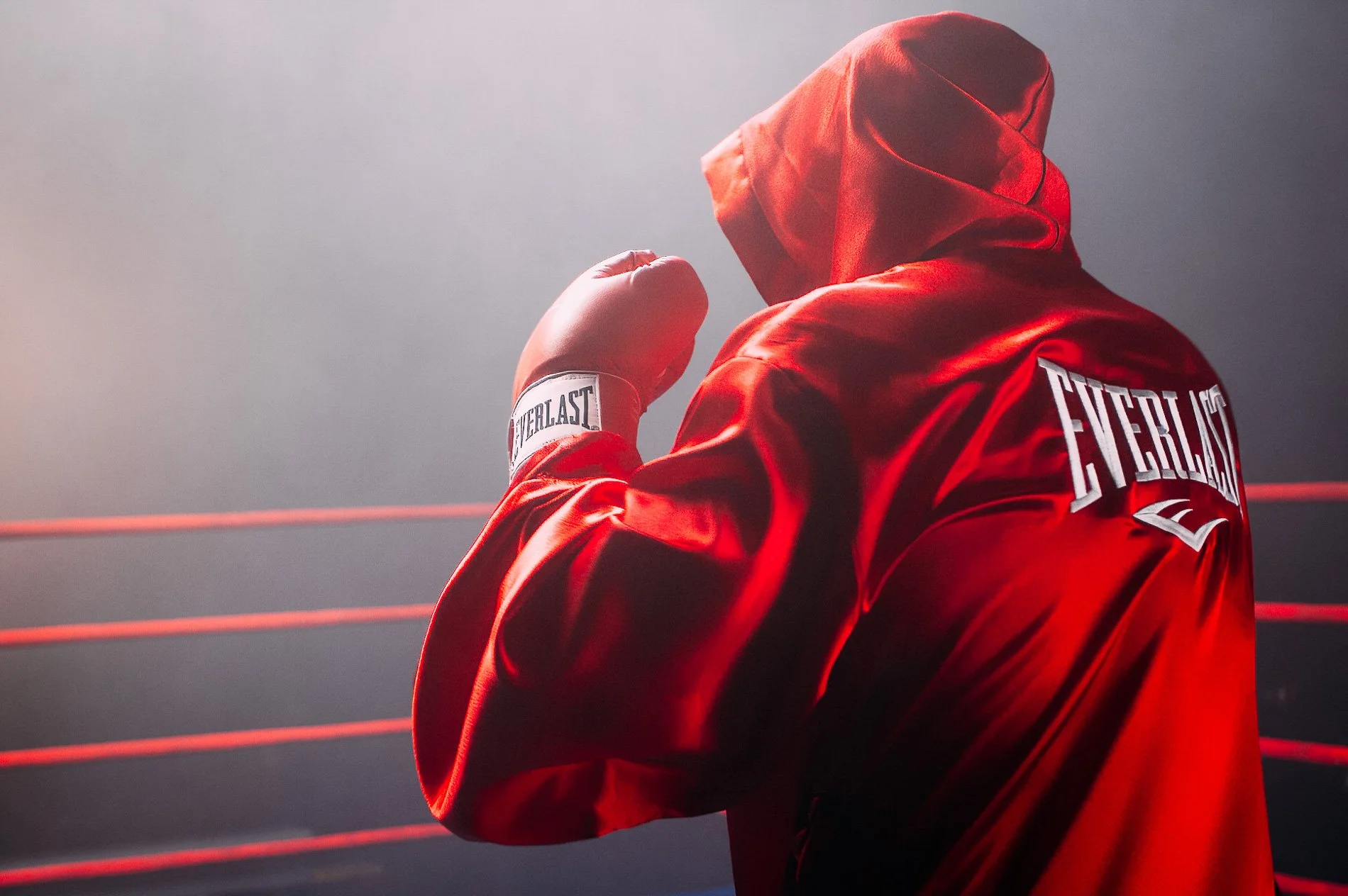 Boxer in a red robe and gloves standing inside a boxing ring during an Everlast Boxing photoshoot.