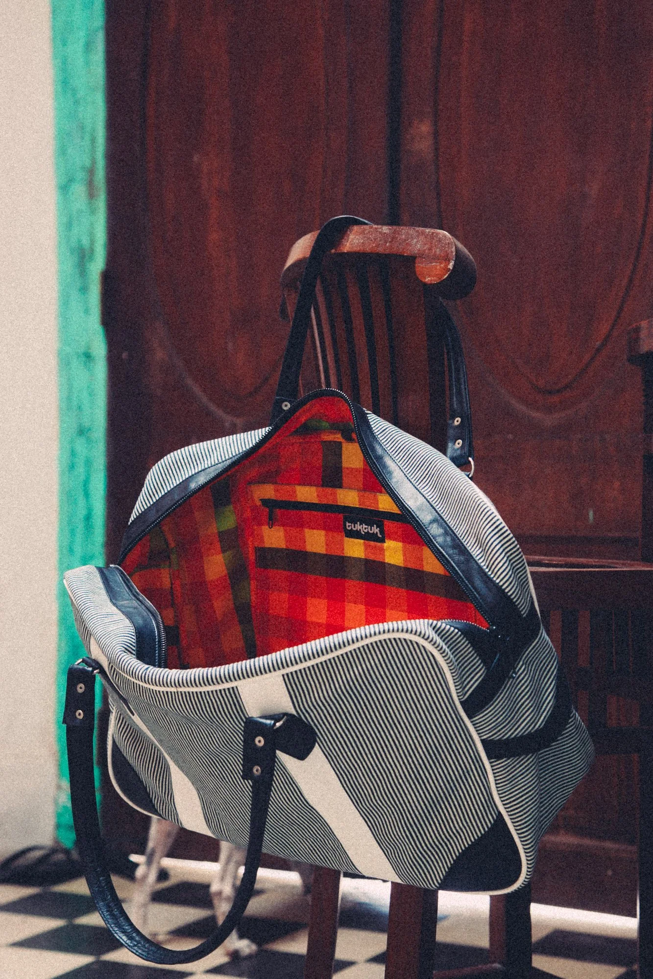 A travel bag rests on a wooden chair during a lifestyle product photography shoot.