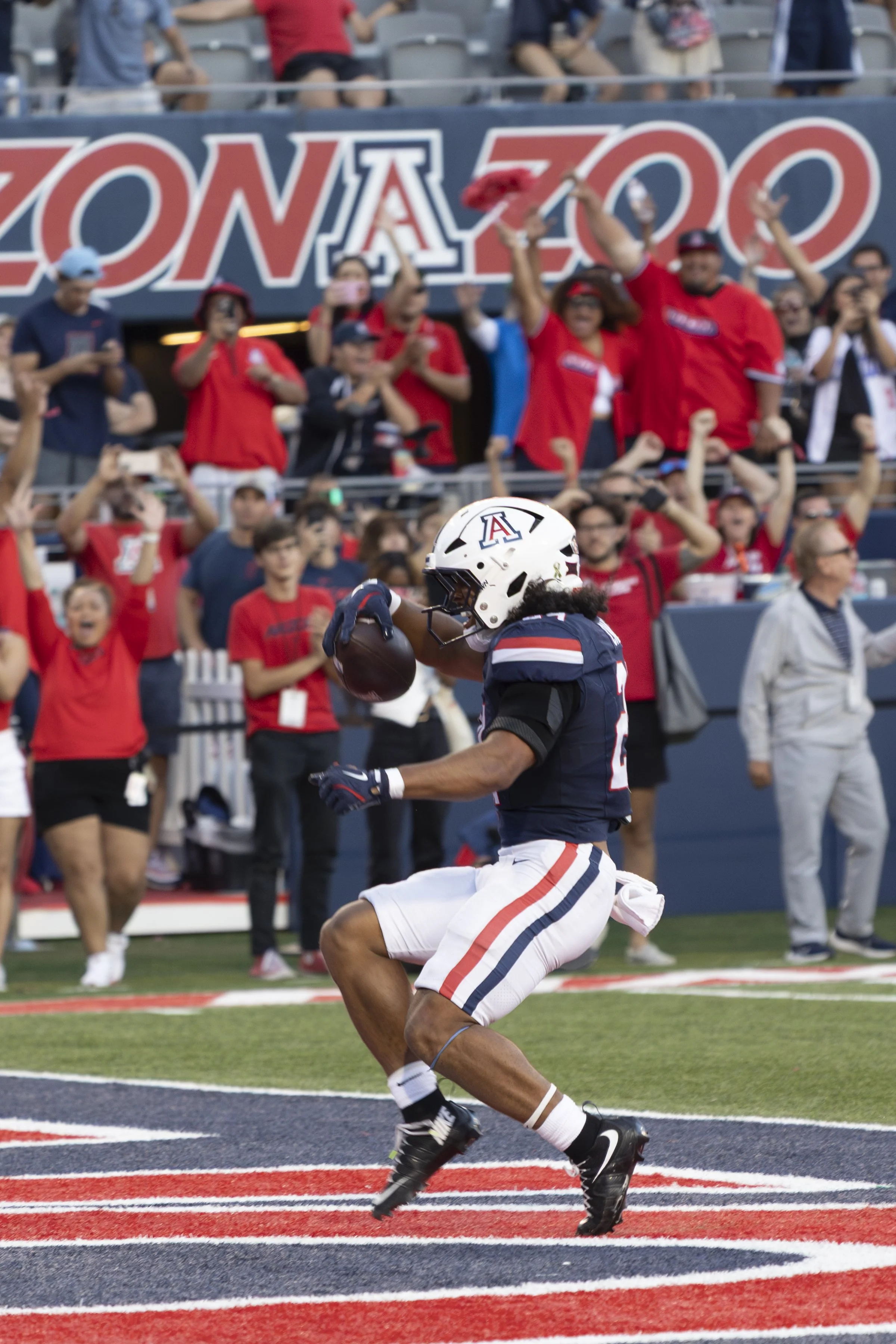 A football player from the University of Arizona catches a football in the end zone as fans cheer in the background at a college football game.