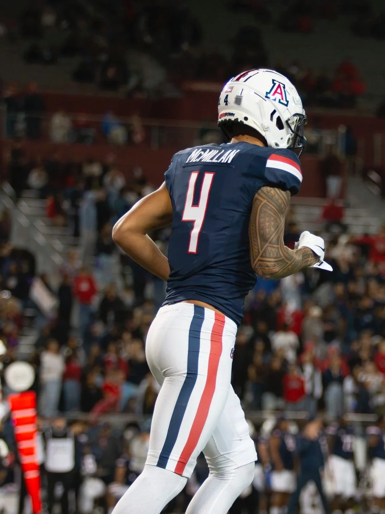 An American football player wearing an Arizona Wildcats uniform with the number 4 is running on the field during a game, with spectators in the background.
