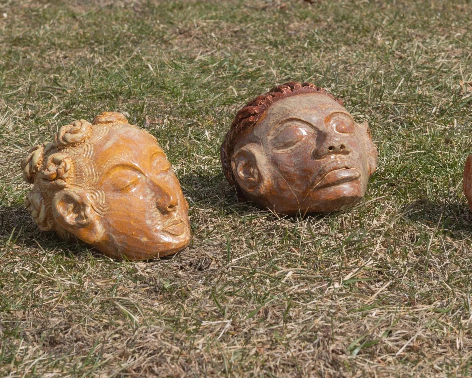 Two carved stone sculptures of human faces lying on dry grass outdoors.