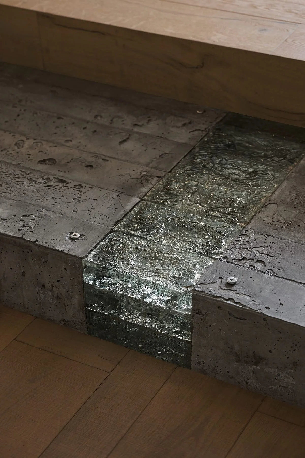 Close-up of a step with wood and concrete materials, featuring a decorative metallic strip on the edge, on a wooden floor.