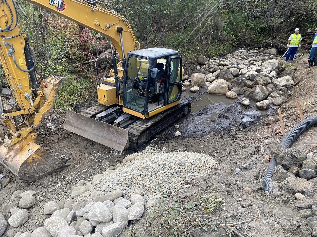 Excavator and crew grading the gravel creekbed during construction