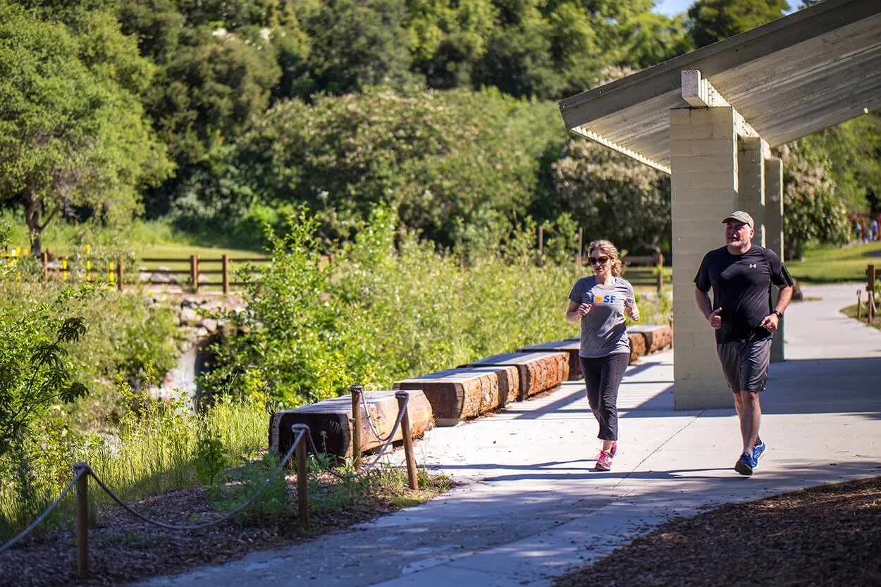 Two people jogging on a paved trail beside Sausal Creek