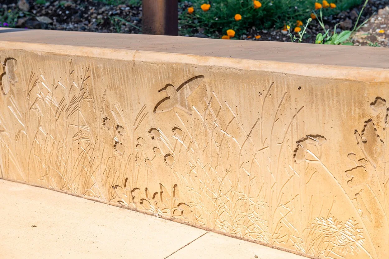 Cast concrete wall with native grass impressions beside California poppies