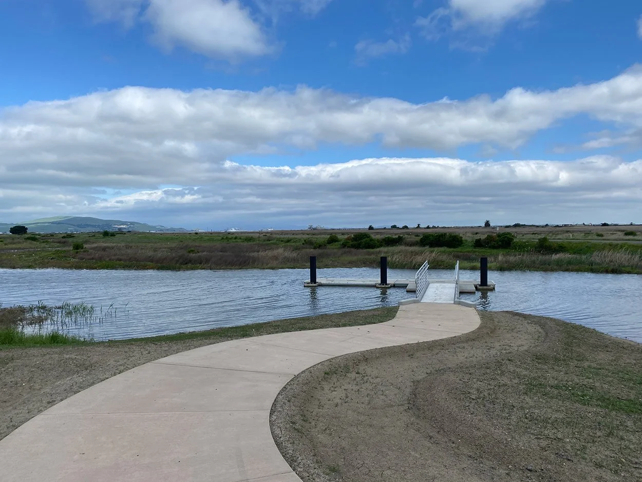 Paved path curving toward a footbridge at the edge of Pacheco Marsh
