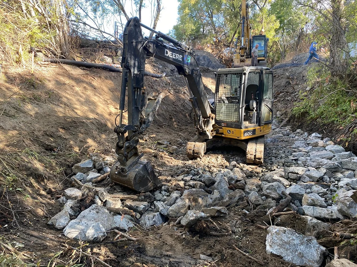 Excavator placing boulders in the creek channel during fish passage construction