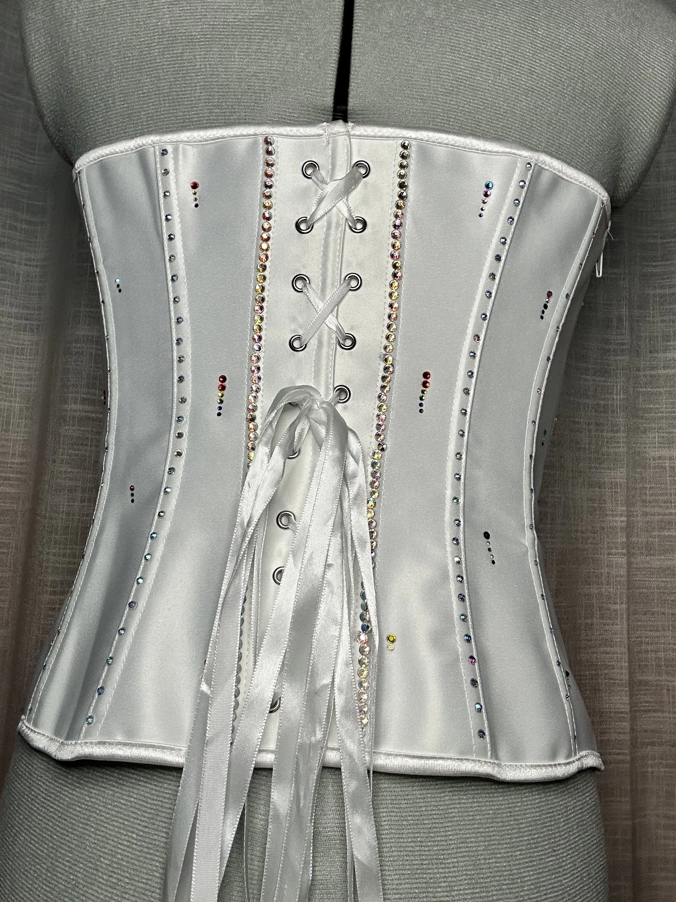 Close-up of a white satin corset adorned with multicolored rhinestones, laced with white satin ribbons.