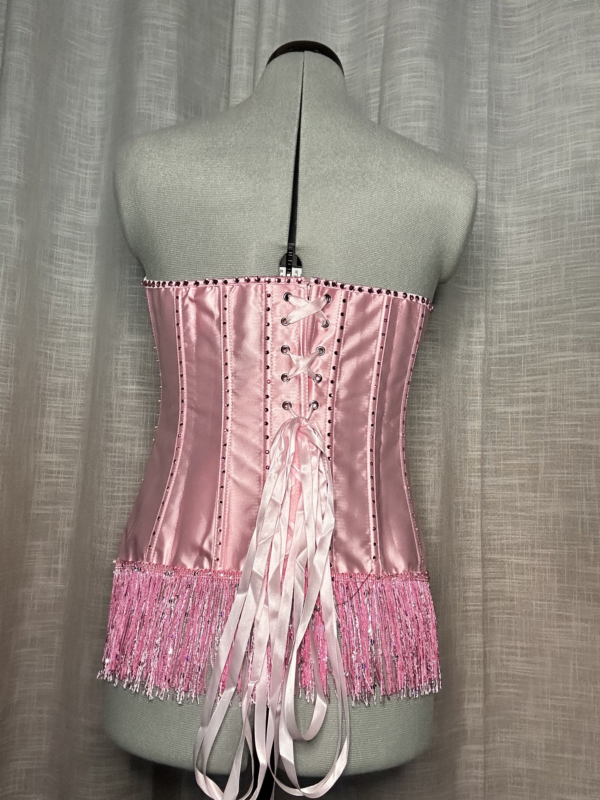 A pink satin corset with lace-up front detail and decorative beading, worn on a mannequin.