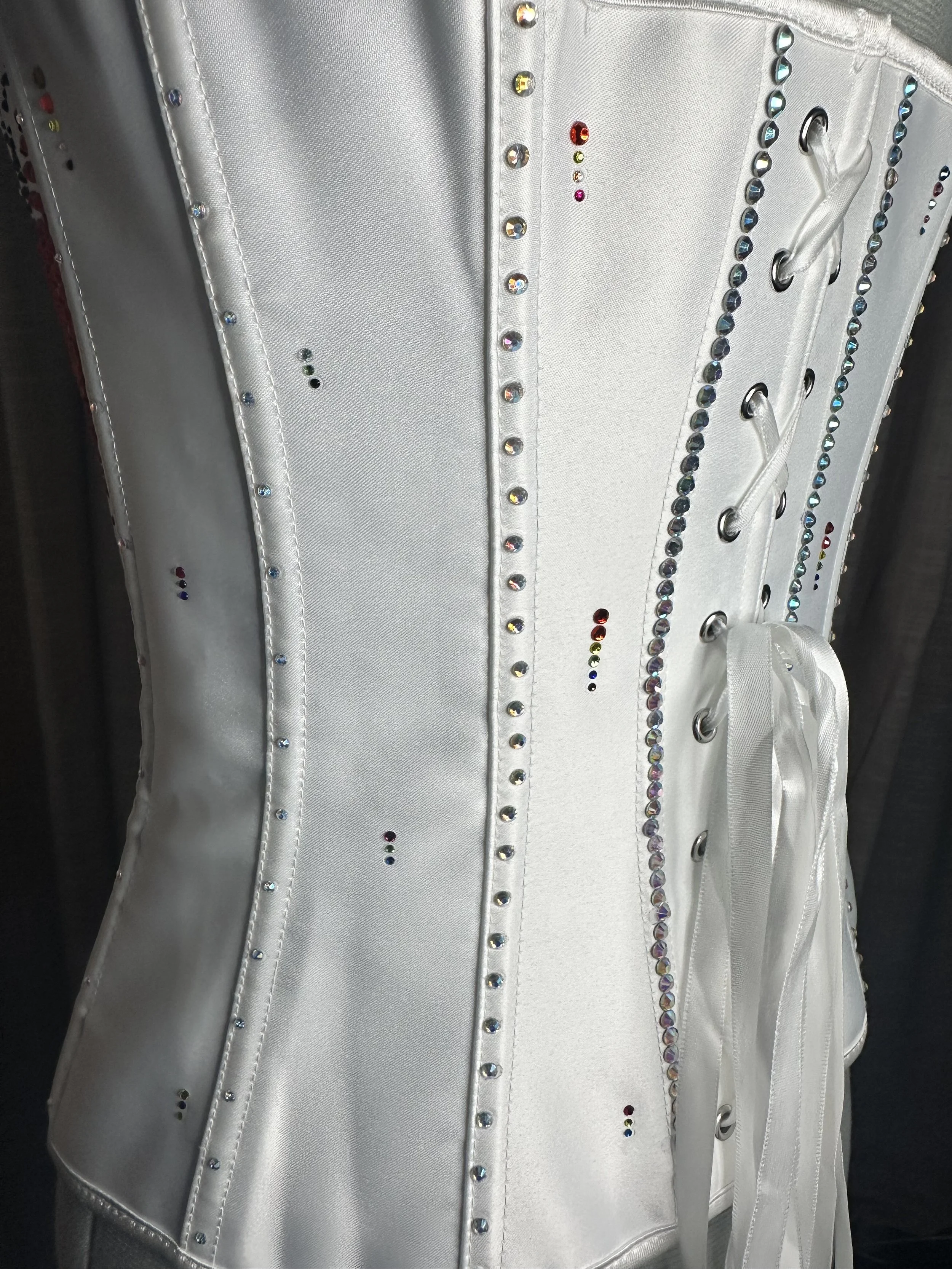 Close-up of a silver or white corset adorned with multicolored rhinestones and laces.