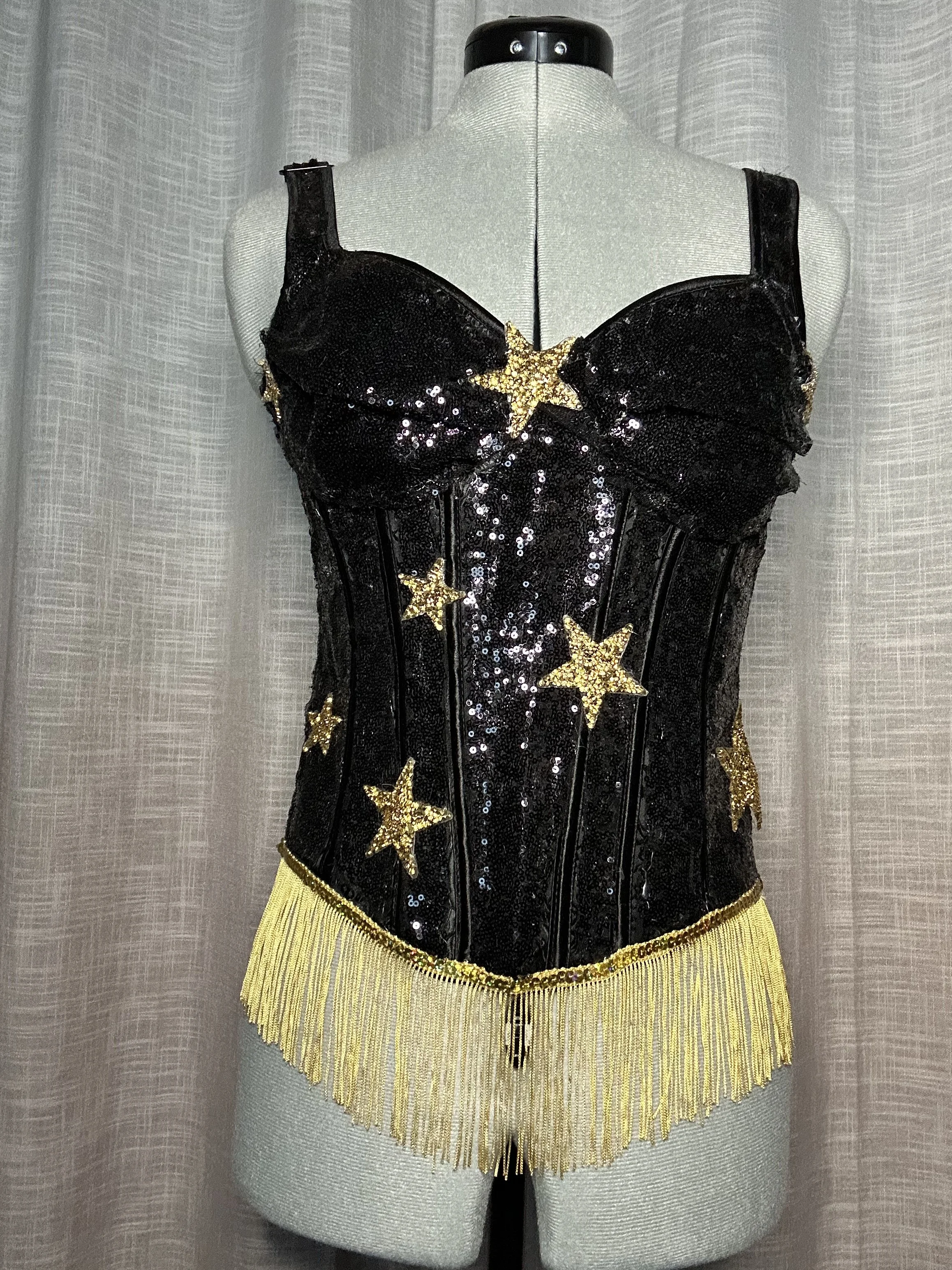 A black sequined costume with gold star accents and gold fringe at the bottom, displayed on a mannequin.