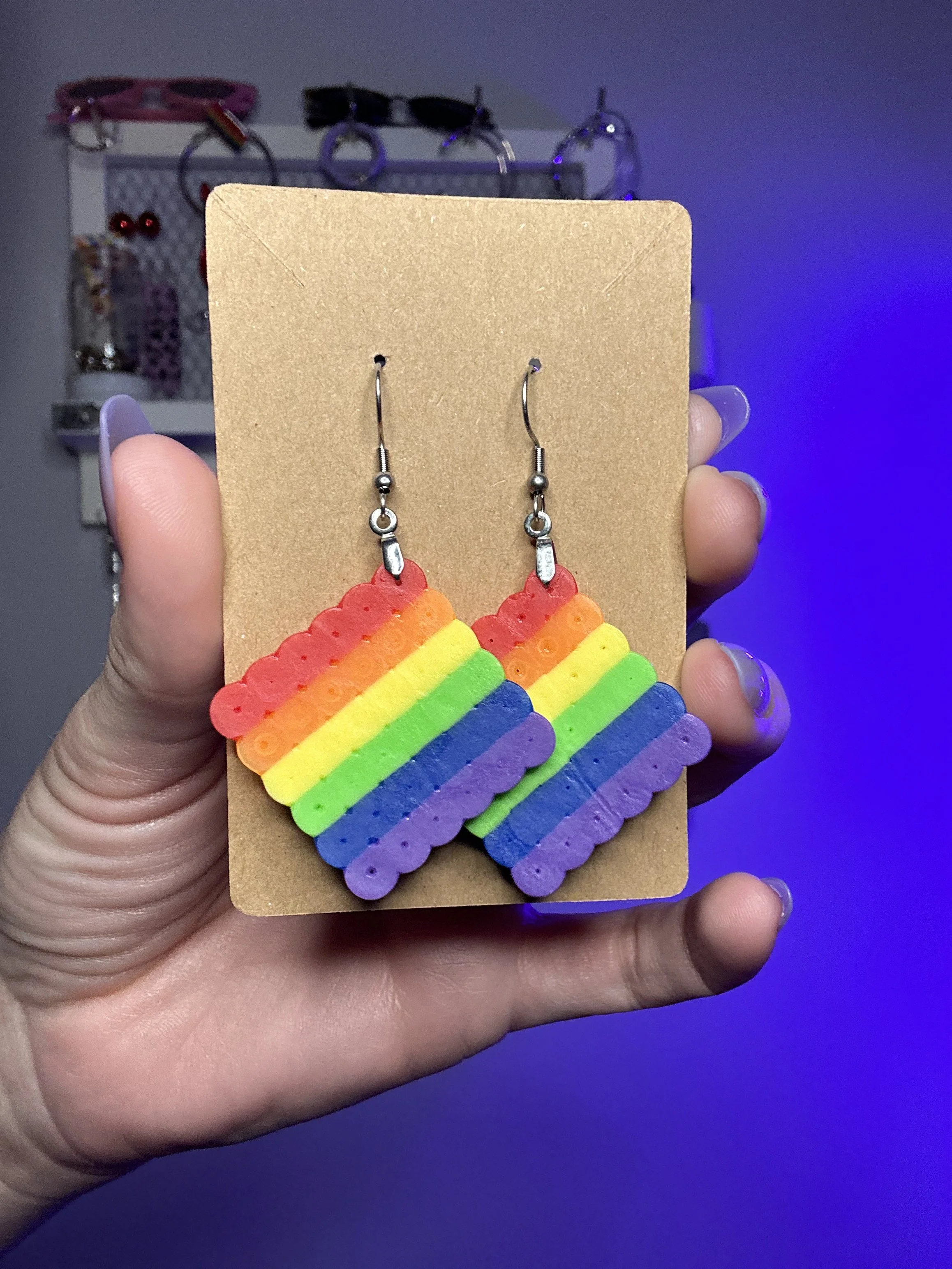 Colorful rainbow-shaped earrings with a hook, displayed on brown cardboard.