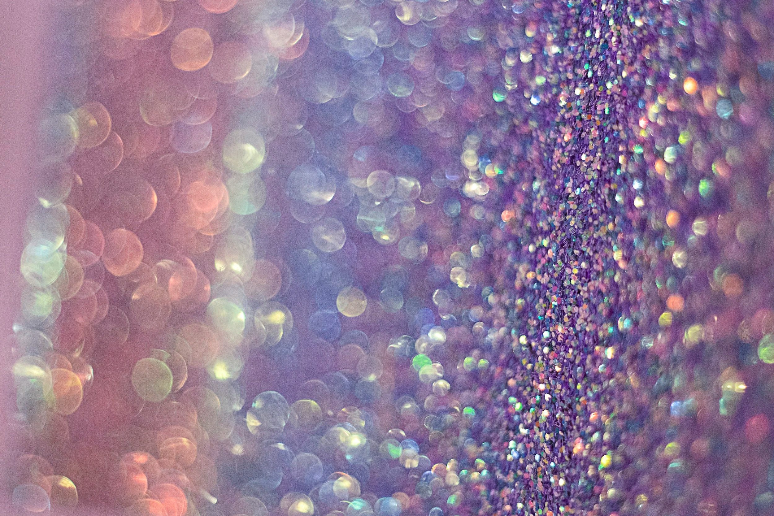 Close-up of colorful glitter and bokeh light effects in purple, pink, and multicolor tones.