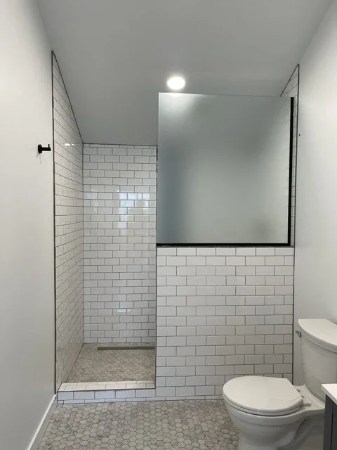Modern bathroom with white subway tile walls, a walk-in shower with a glass partition, a round toilet, and a hexagonal tile floor.