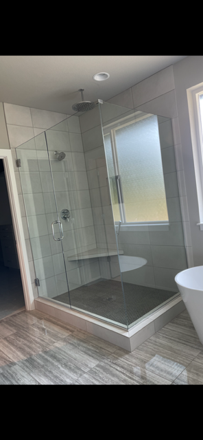 Modern glass-enclosed walk-in shower with a rain showerhead, mounted on a tiled wall, and a window adjacent to the shower.