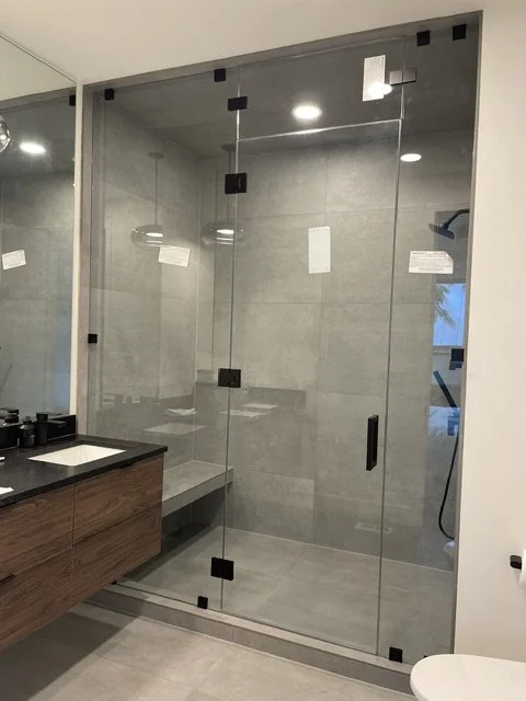 Modern bathroom with glass shower enclosure, gray tiles, wooden vanity, and a mirror.