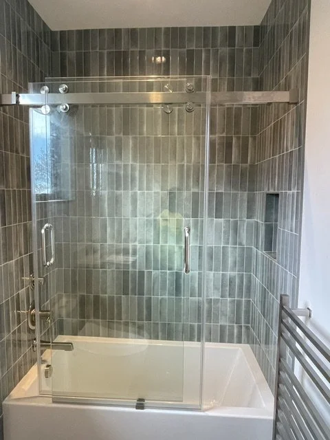 Glass shower enclosure with sliding doors inside a tiled bathroom shower area.