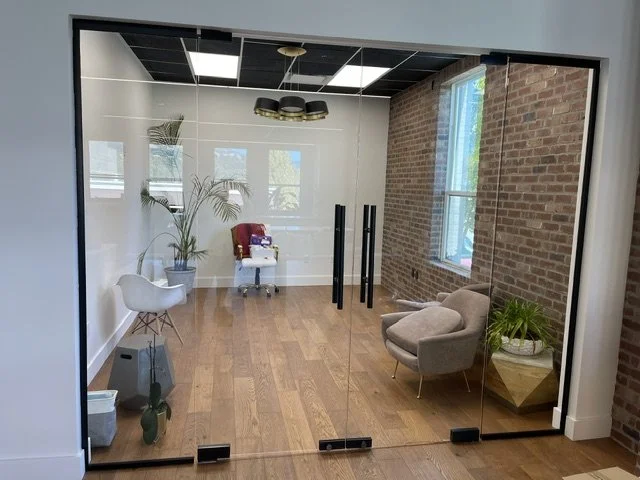 Modern office with glass door, hardwood floor, brick wall, and two chairs near window