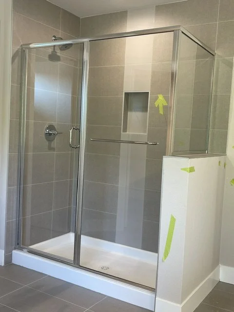 Modern glass shower enclosure with gray tiled walls, a built-in niche, and a metal grab bar, in a bathroom under renovation.