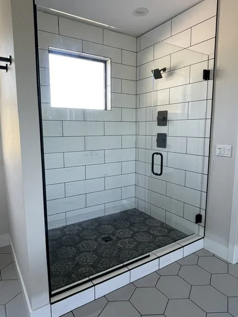 Empty walk-in shower with white subway tile walls, black fixtures, a small window, and a mosaic tile floor.