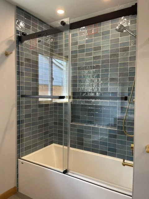 Bathroom with a bathtub, tile walls, a glass shower enclosure, and a window.