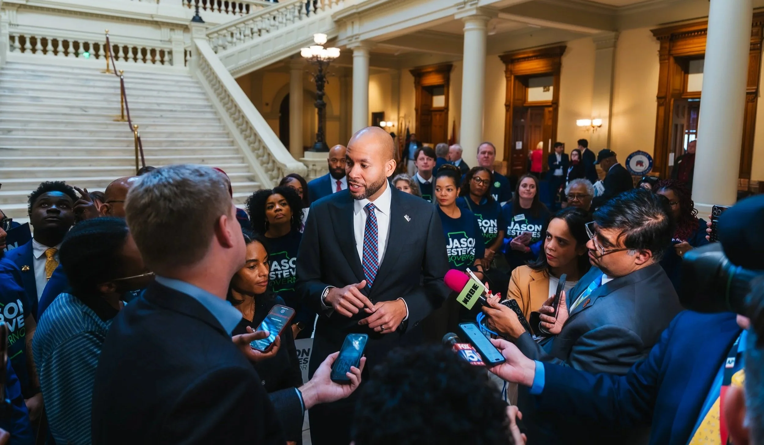 Georgia's Jason Esteves speaking to a group of reporters and journalists in a large government building with marble stairs and columns.