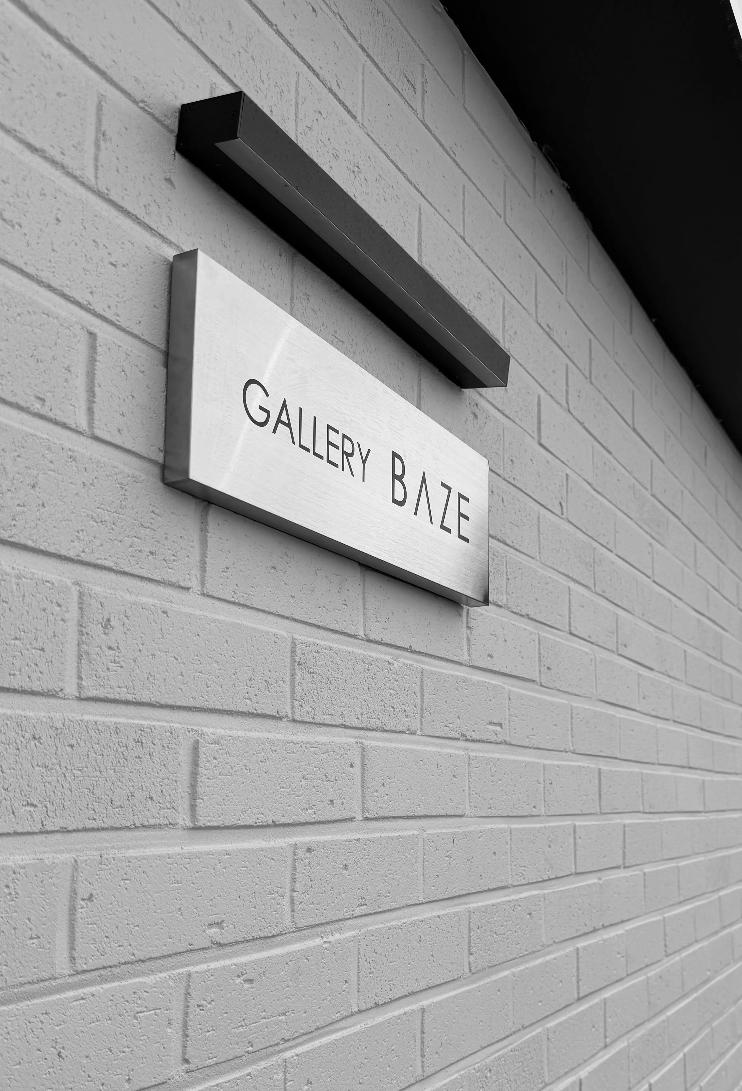 흰 벽에 설치된 'GALLERY BAZE'라는 간판이 있는 외부 건물 모습.