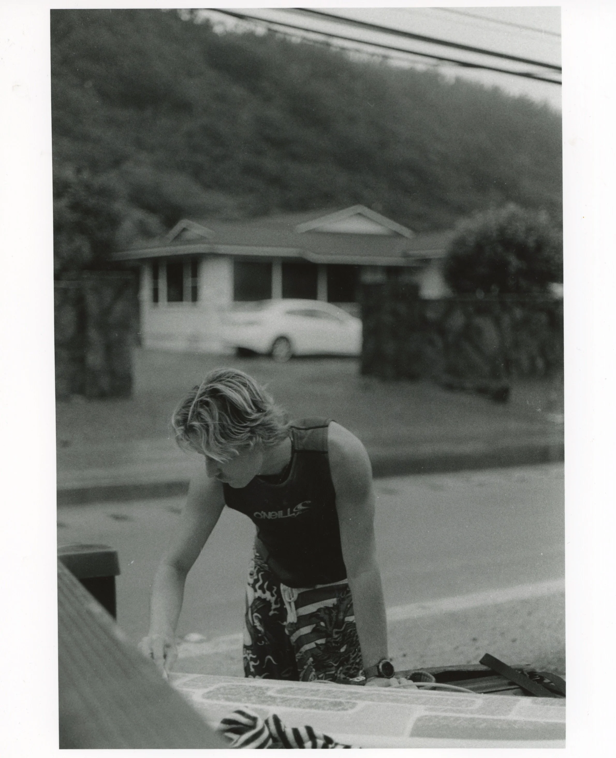 Guy Waxing Surfboard, 2026, Gelatin Silver Print from a B&W 35mm negative, 8” x 10”