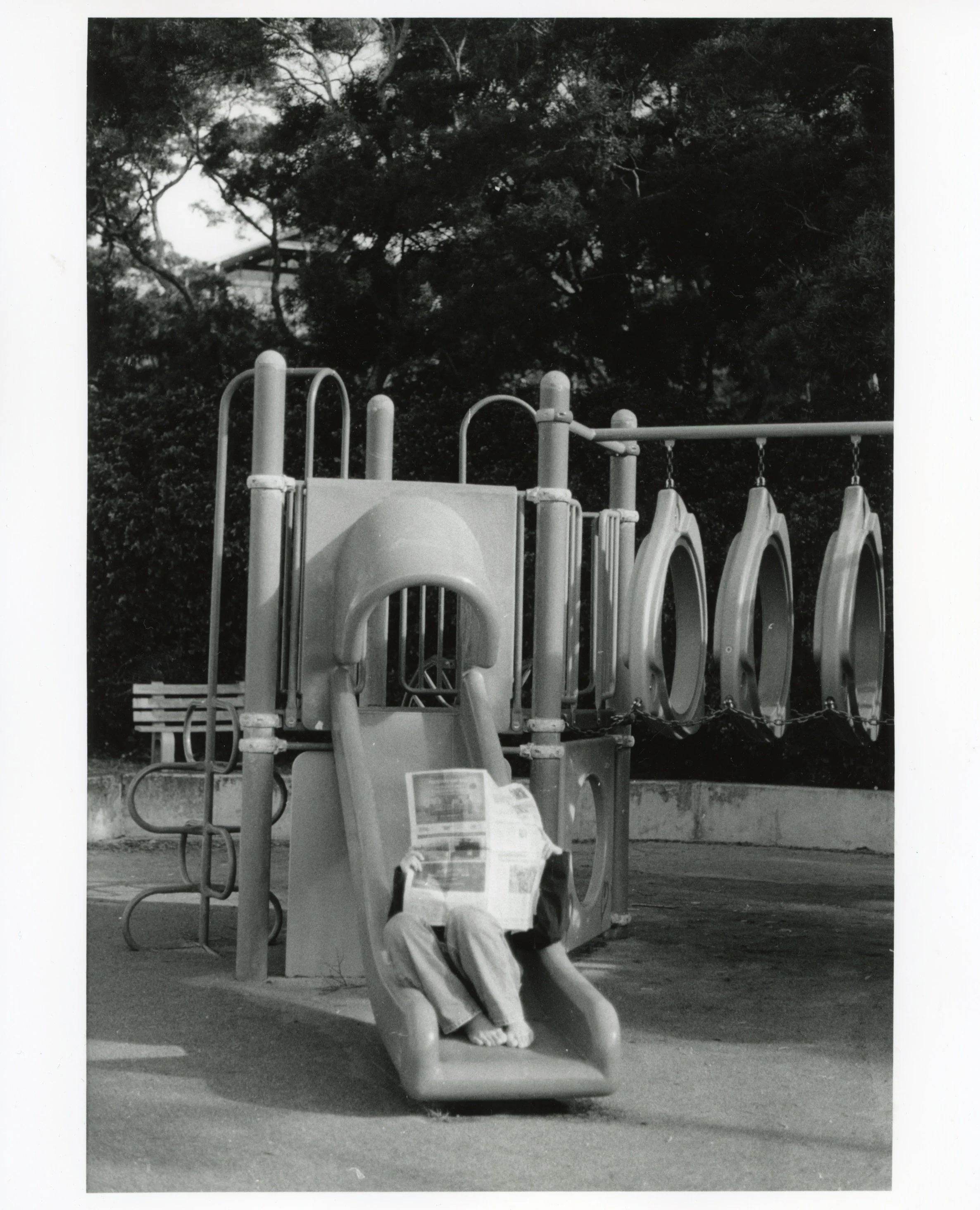 Girl Reading Newspaper on Slide, 2026, Gelatin Silver Print from a B&W 35mm negative, 8” x 10”
